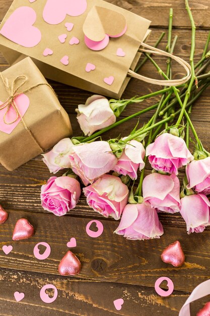 Rosas rosas y regalo envuelto en papel reciclado sobre mesa de madera rústica.