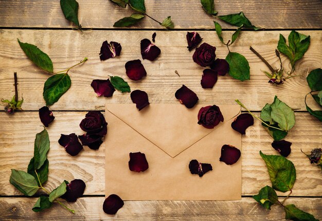 Rosas secas sobre un fondo de madera y un sobre postal. Una carta romántica entre los pétalos. Herbario y flores secas.