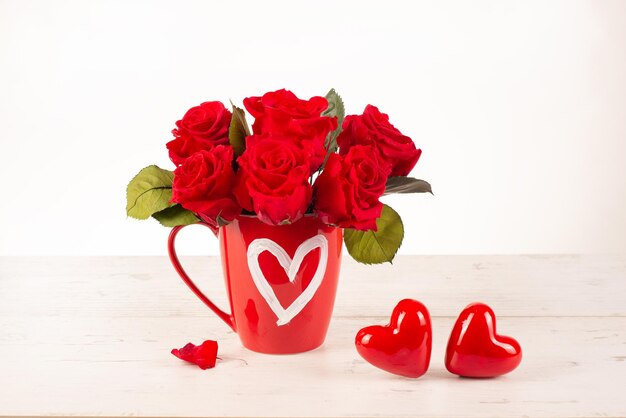 Rosas en una taza con un corazón dibujado en una mesa con corazones decorativos Concepto festivo Día de San Valentín