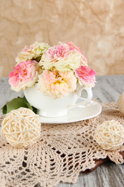 Rosas en taza sobre servilletas sobre mesa de madera sobre fondo beige