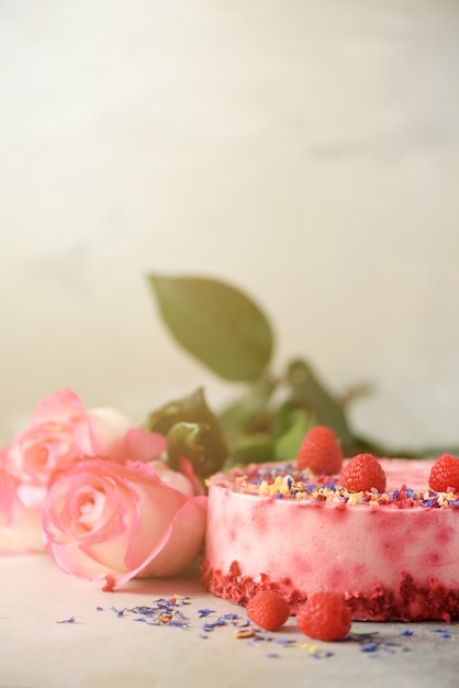 Las rosas y la torta rosadas de la frambuesa con las bayas frescas, romero, secan las flores en fondo concreto. Concepto de fiesta de cumpleaños