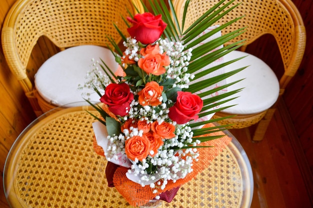 Rosas vermelhas e amarelas em um buquê com flores brancas intercaladas em uma mesa ao lado de cadeiras