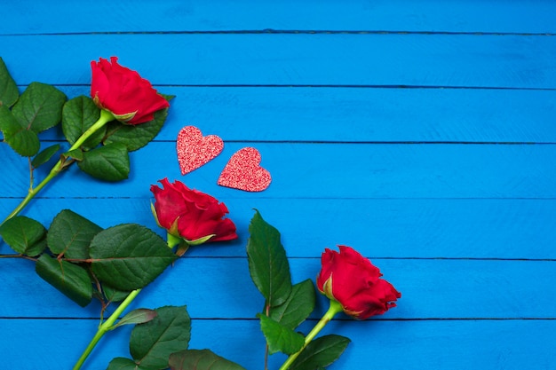 Rosas vermelhas e dois corações vermelhos na mesa de madeira azul.