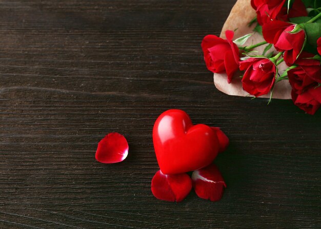 Rosas vermelhas embrulhadas em papel com coração no fundo da mesa de madeira