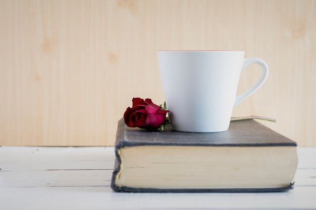 Rose, libro y taza de café en la mesa de madera blanca