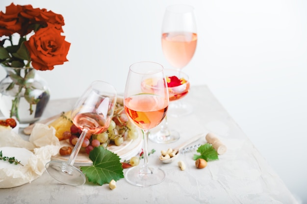 Rose Wein in verschiedenen Weingläsern Flasche auf weißem Tisch mit Trauben Käse, Snacks Blumenstrauß. modernes Stillleben Rose Wine Komposition auf hellgrauem Betonhintergrund.