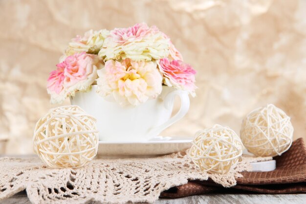 Rosen in Tasse auf Servietten auf Holztisch auf beigem Hintergrund
