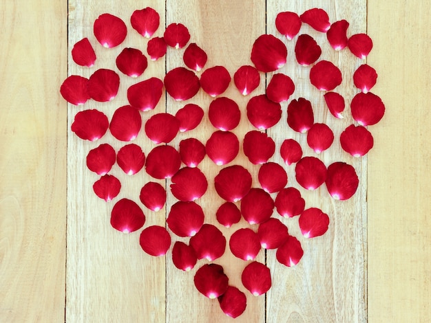 Rosenblätter angeordnet in einer Herzform auf einem hölzernen Hintergrund.