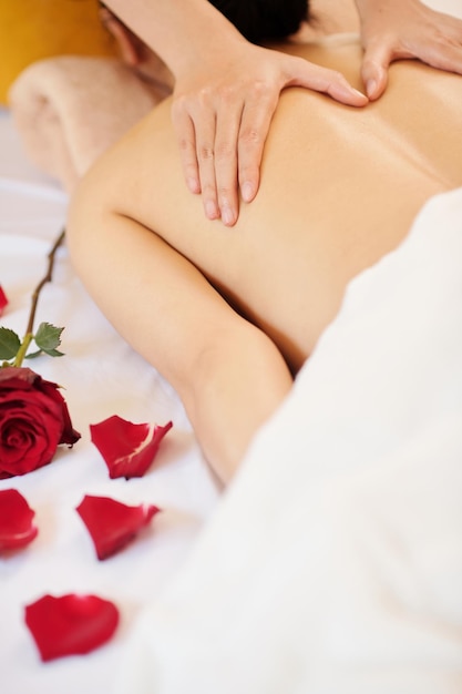 Rosenblüte auf dem Bett neben einer jungen Frau, die eine entspannende Rückenmassage bekommt