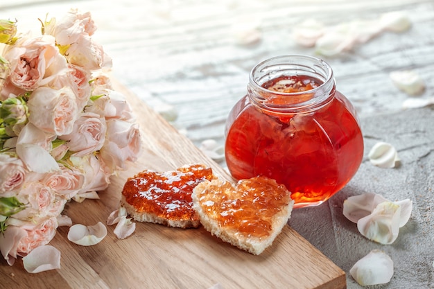 Rosenblütenmarmelade und herzförmiges Sandwich mit Marmeladenrosenblume auf Tisch.