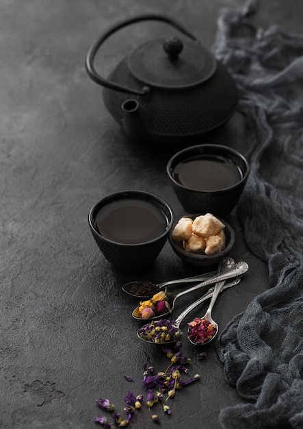 Rosenknospen, blaue Malvenblüten, grüner und schwarzer loser Tee mit Zucker und chinesische Teekanne mit Löffeln und zwei Tassen