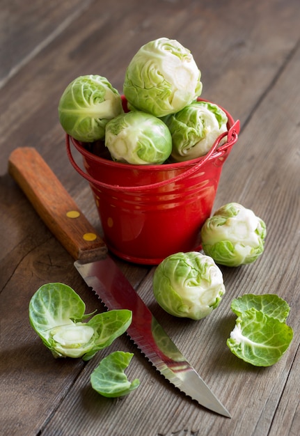 Rosenkohl in einem roten Eimer mit Messer auf Holztisch nah oben