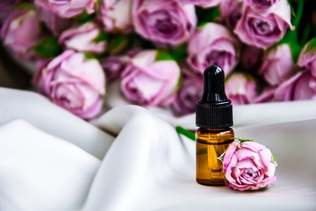 Rosenöl. Spa- und Aromatherapie-Rosenblumen-Flasche mit ätherischem Öl mit Pipette auf satiniertem champagnerfarbenem Stoff. Flaschen ätherisches Rosenöl und frische Blumen. Platz kopieren