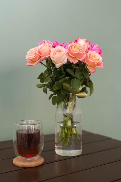 Rosenstrauß mit Glas Tee auf einem Holztisch auf grünem Hintergrund