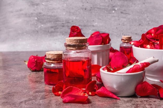 Rosenwasser mit Rosenblättern. Herstellung von Bio-Rosenessenz zum Kochen von Kerala Indien. Aromatherapie, Spa-Entspannung, Kosmetikkonzept. Modernes hartes Licht, dunkler Schatten. Steinhintergrund, Kopienraum
