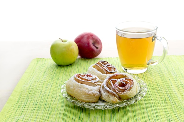 Rosetas de maçãs em chá de massa folhada e duas maçãs em uma mesa fechada