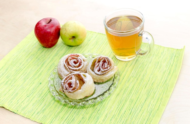 Rosetas de manzanas en té de hojaldre y dos manzanas en un primer plano de la mesa