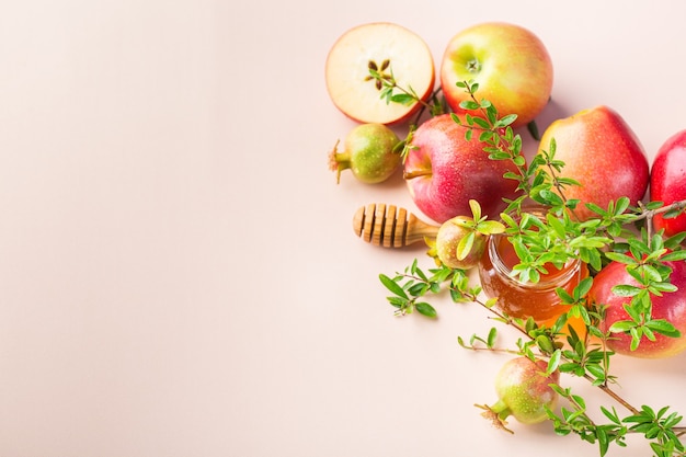 Rosh Hashaná, concepto de vacaciones de año nuevo judío con símbolos tradicionales, manzanas, miel, granada en una mesa de color rosa pastel, albaricoque. Copiar el fondo del espacio