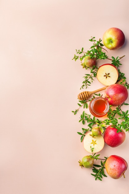 Rosh Hashaná, concepto de vacaciones de año nuevo judío con símbolos tradicionales, manzanas, miel, granada en una mesa de color rosa pastel, albaricoque. Endecha plana, copia de fondo del espacio