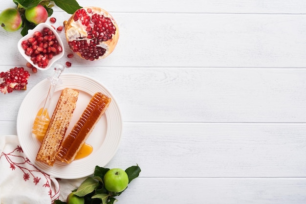 Rosh Hashaná Tarro de miel panal de manzana y granada en la mesa de fondo rústico antiguo de madera blanca Tarjeta de felicitación de vacaciones de Año Nuevo judío Atributos de vacaciones de Rosh Hashaná Espacio para texto