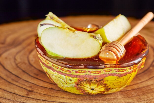 Rosh hashanah - jüdisches Neujahrsfeiertagskonzept. Schüssel mit Honig und geschnittenen Äpfeln auf einem Holzständer.