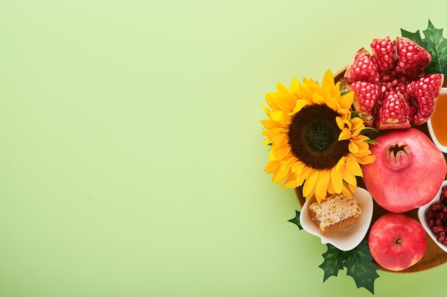 Rosh Hashanah Miel de manzana de granada madura y flores amarillas de girasol en composición de fondo verde con símbolos atributos de vacaciones judías de Rosh Hashanah Vista superior con espacio de copia