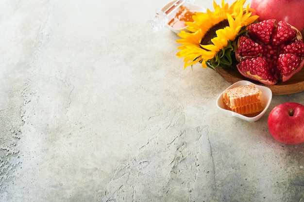 Rosh Hashanah Reifer Granatapfelhonig und sonnenblumengelbe Blumen auf rustikalem grauem Hintergrund Komposition mit Symbolen Herbst jüdische Rosh Hashanah Feiertagsattribute Draufsicht mit Kopierbereich