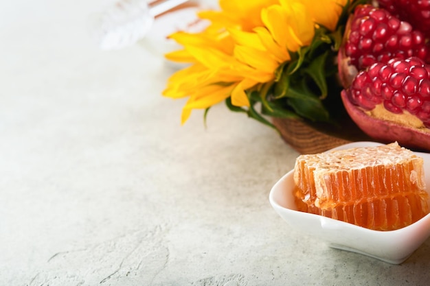 Rosh Hashanah Reifer Granatapfelhonig und sonnenblumengelbe Blumen auf rustikalem grauem Hintergrund Komposition mit Symbolen Herbst jüdische Rosh Hashanah Feiertagsattribute Draufsicht mit Kopierbereich