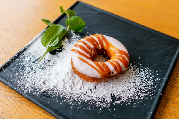 Rosquilla de caramelo con chispas de azúcar en un plato cuadrado negro Delicioso postre con una rodaja de menta