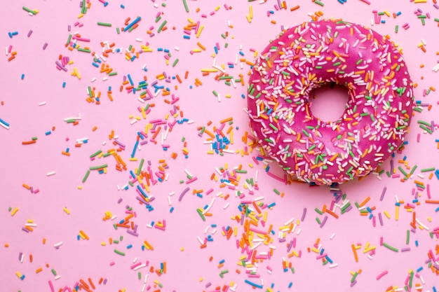 Rosquilla dulce rosa con chispas multicolores sobre una superficie plana de color rosa