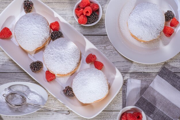 Rosquilla rellena de gelatina berlinesa con frambuesa y mora sobre fondo de madera.