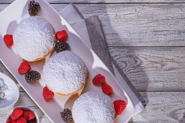 Rosquilla rellena de gelatina berlinesa con frambuesa y mora sobre fondo de madera.