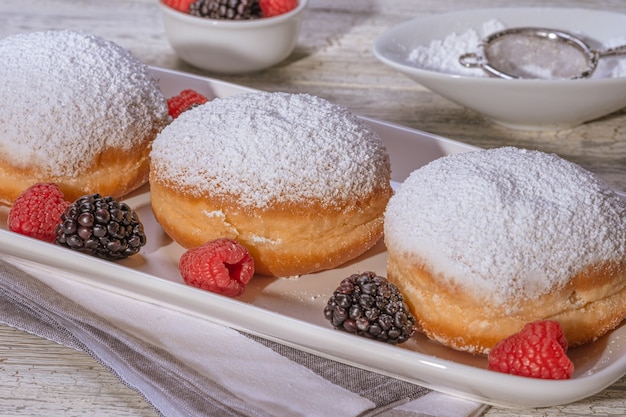 Rosquilla rellena de gelatina berlinesa con frambuesa y mora sobre fondo de madera.