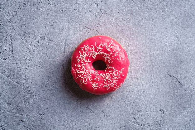 Rosquilla rosa con chispas, postre dulce glaseado sobre fondo con textura de hormigón, vista superior