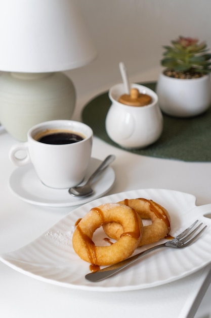 Rosquillas de azúcar en polvo frescas con chocolate y taza de café en la mesa de madera en la cafetería