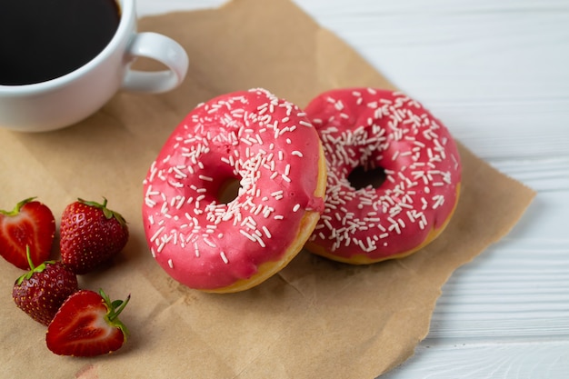 Foto rosquillas caseras recién horneadas con glaseado de fresa y café negro.