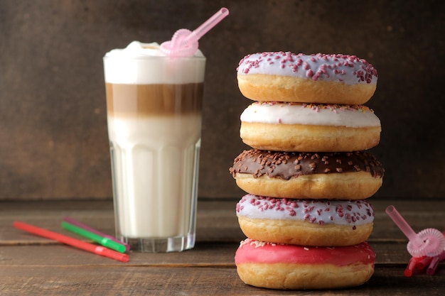 Rosquillas dulces variadas con glaseado y coberturas y café con leche en una mesa de madera marrón