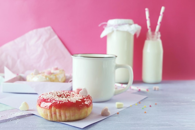 Rosquillas recién horneadas glaseadas y espolvoreadas con corazones de caramelo, leche y yogur en una taza