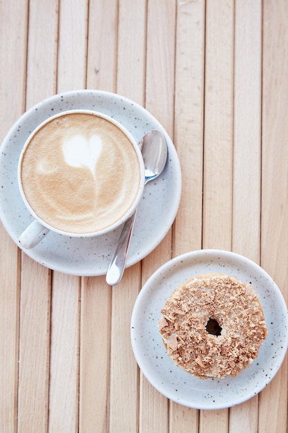 Rosquinha natural sem açúcar e cappuccino em xícara de cerâmica branca na mesa de madeira no terraço Café da manhã estético Comida de vista superior