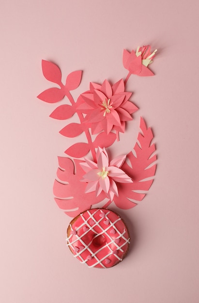 Rosquinha rosa com confeiteiro e artesanato de papel origami decoração de flores modernas, em fundo rosa, monocromático