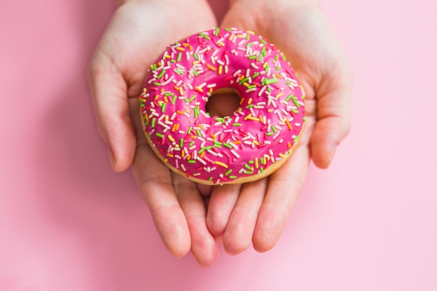 Rosquinha rosa em mãos no fundo rosa. mulher segurando rosquinha rosa