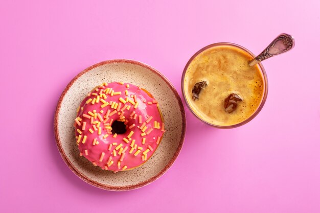 Rosquinha rosa em um prato e café gelado, vista superior, em um rosa.