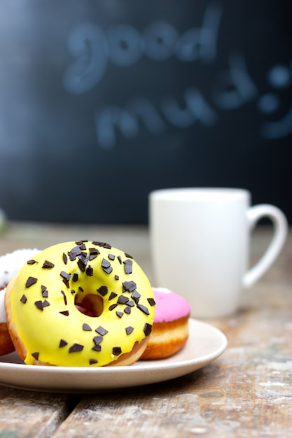 Rosquinhas coloridas em um prato com uma xícara de café em uma mesa de madeira café da manhã em uma cafeteria aconchegante