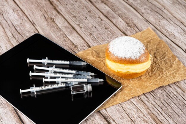 Rosquinhas de creme brasileiras ao lado de várias seringas e ampolas com insulina na vista do lado do tablet