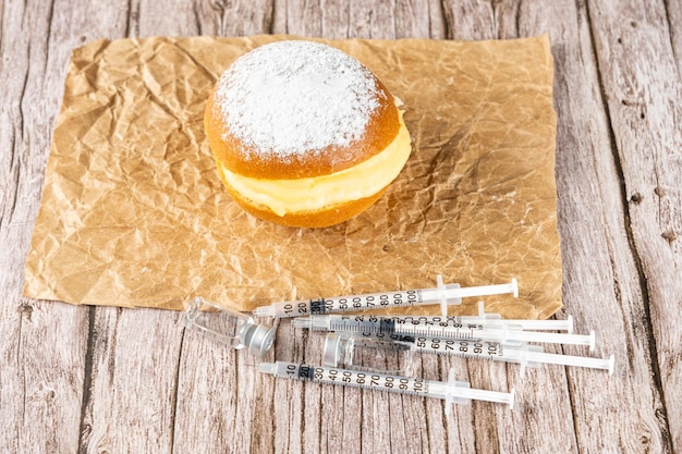 Rosquinhas de creme brasileiras em papel pardo ao lado de várias seringas e ampolas de insulina