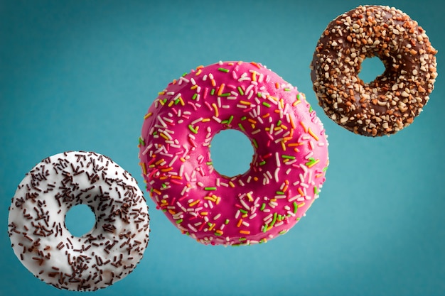 Rosquinhas de vidros doces voando sobre fundo azul, conceito de junk food