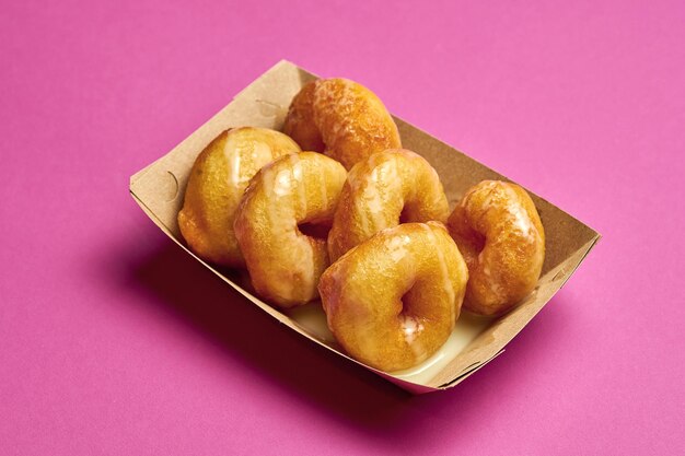 Rosquinhas frescas com molho doce em um fundo rosa.