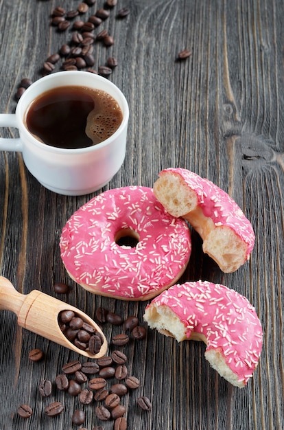 Rosquinhas frescas rosa com granulado e uma xícara de café na velha mesa de madeira