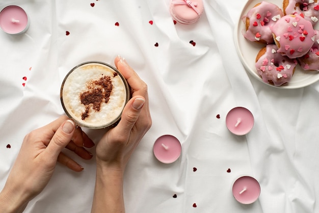 Rosquinhas pequenas na cama branca com uma xícara de café e velas cor de rosa