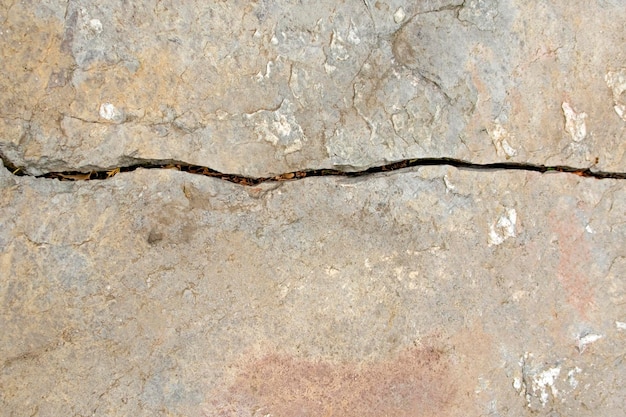 Rostige graue Steinmauer mit einem horizontalen Riss in der mittleren Hintergrundnahaufnahme